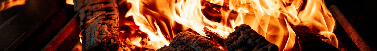 Wood logs burn in an outdoor fireplace.