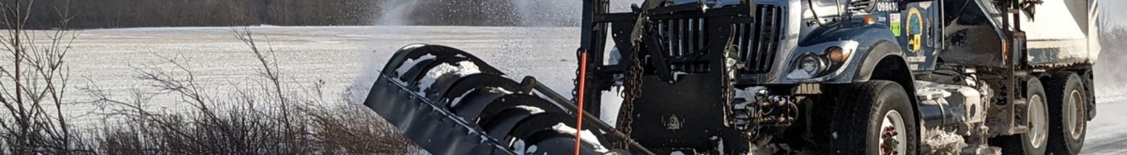 A snow plow truck drives along the road in the winter