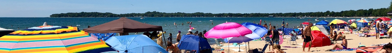 A sandy beach full of people going in and out of a lake