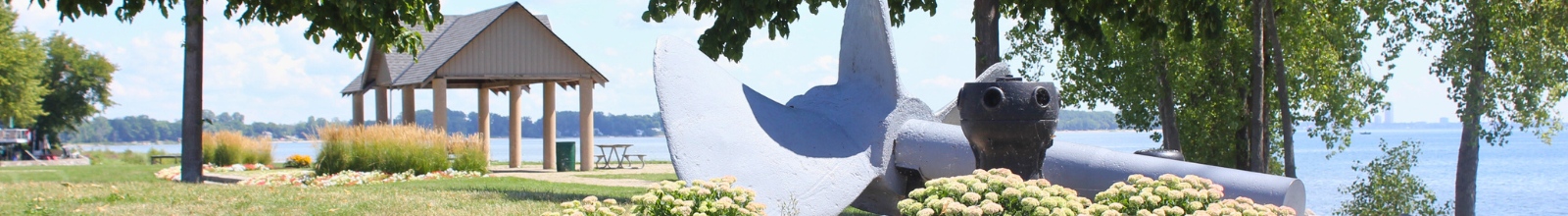 A large ship rudder lays in a bed of flowers in a sunny park