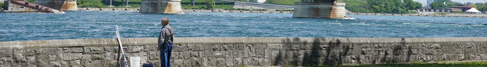 A person stands next to a river break wall with a fishing rod